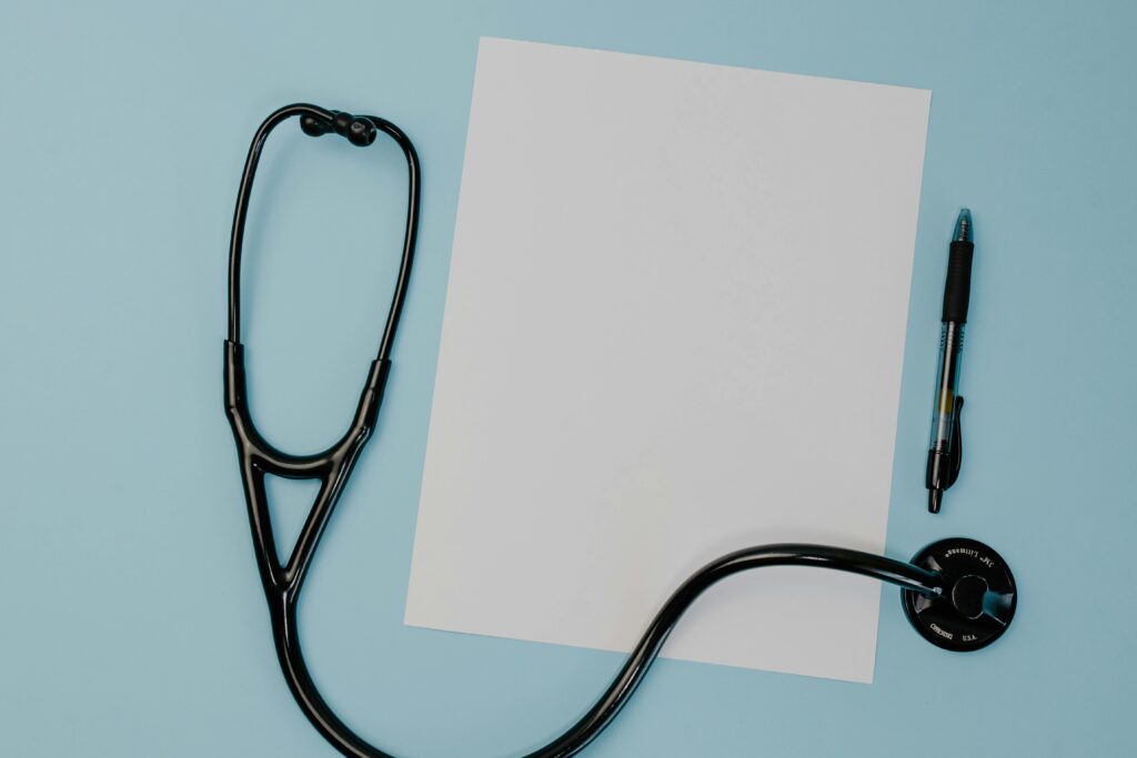 Flat lay of a stethoscope, blank paper, and pen on a blue background.