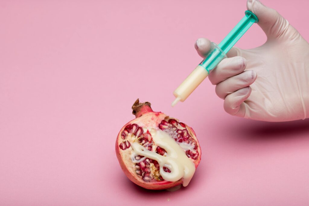 A provocative conceptual image of a pomegranate with a syringe against a pink background.