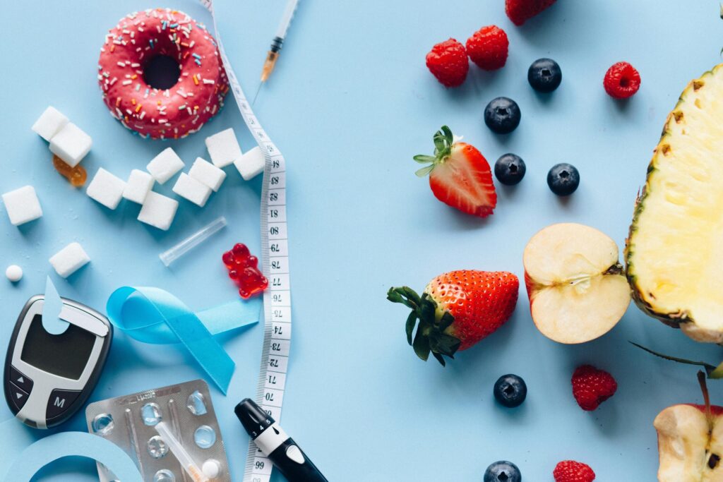 Flatlay of fruits, sugary treats, and diabetes tools on a blue background, symbolizing health choices.